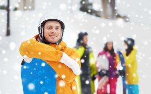 49308290 - winter, leisure, extreme sport, friendship and people concept - happy young man in helmet with snowboard and group of friends